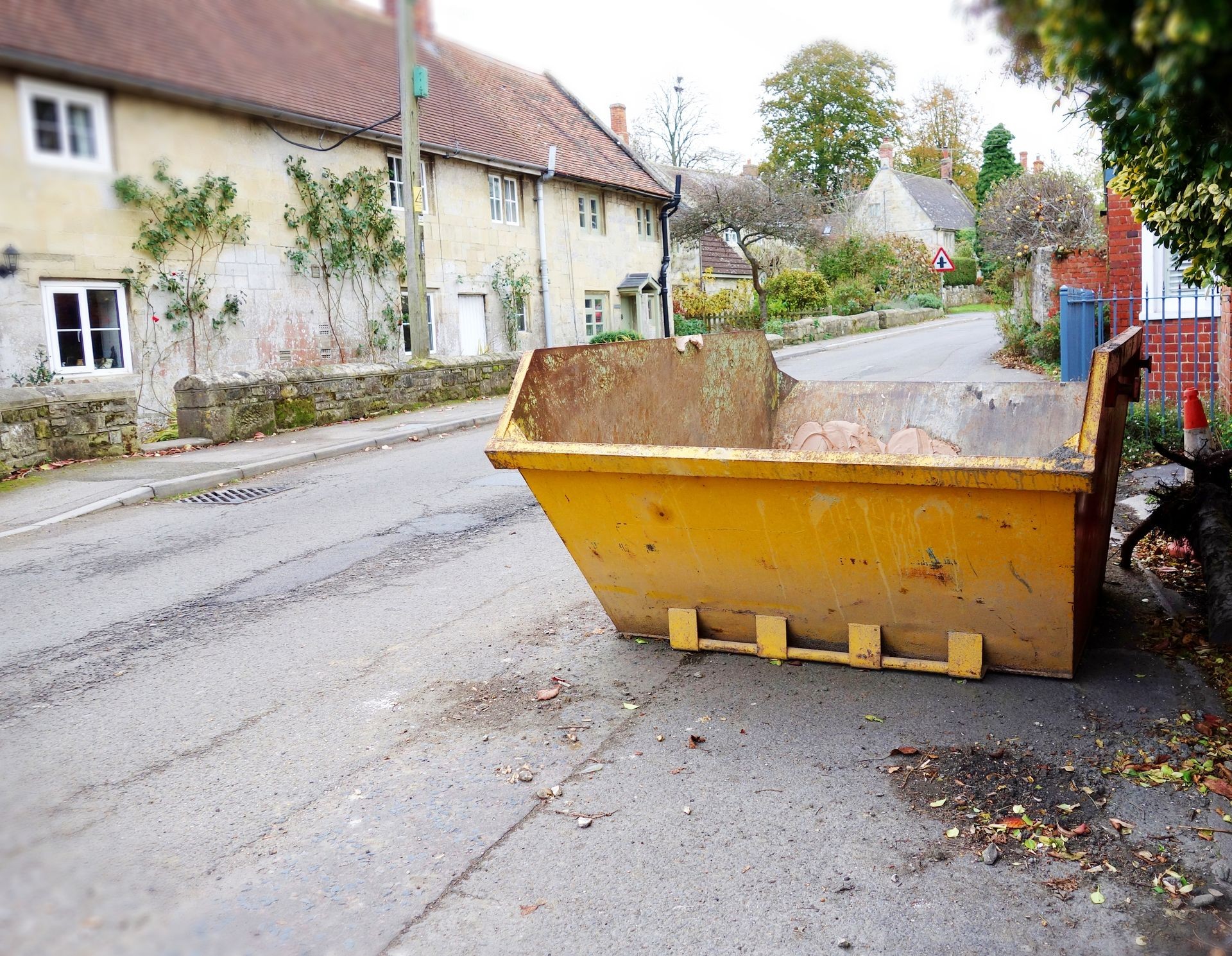 Yellow rubbish skip bin, right side of frame. Photo taken in angle, focus on the bin with space to add text on empty road surface & blurry houses in background. Clearance, renovate, building concept.