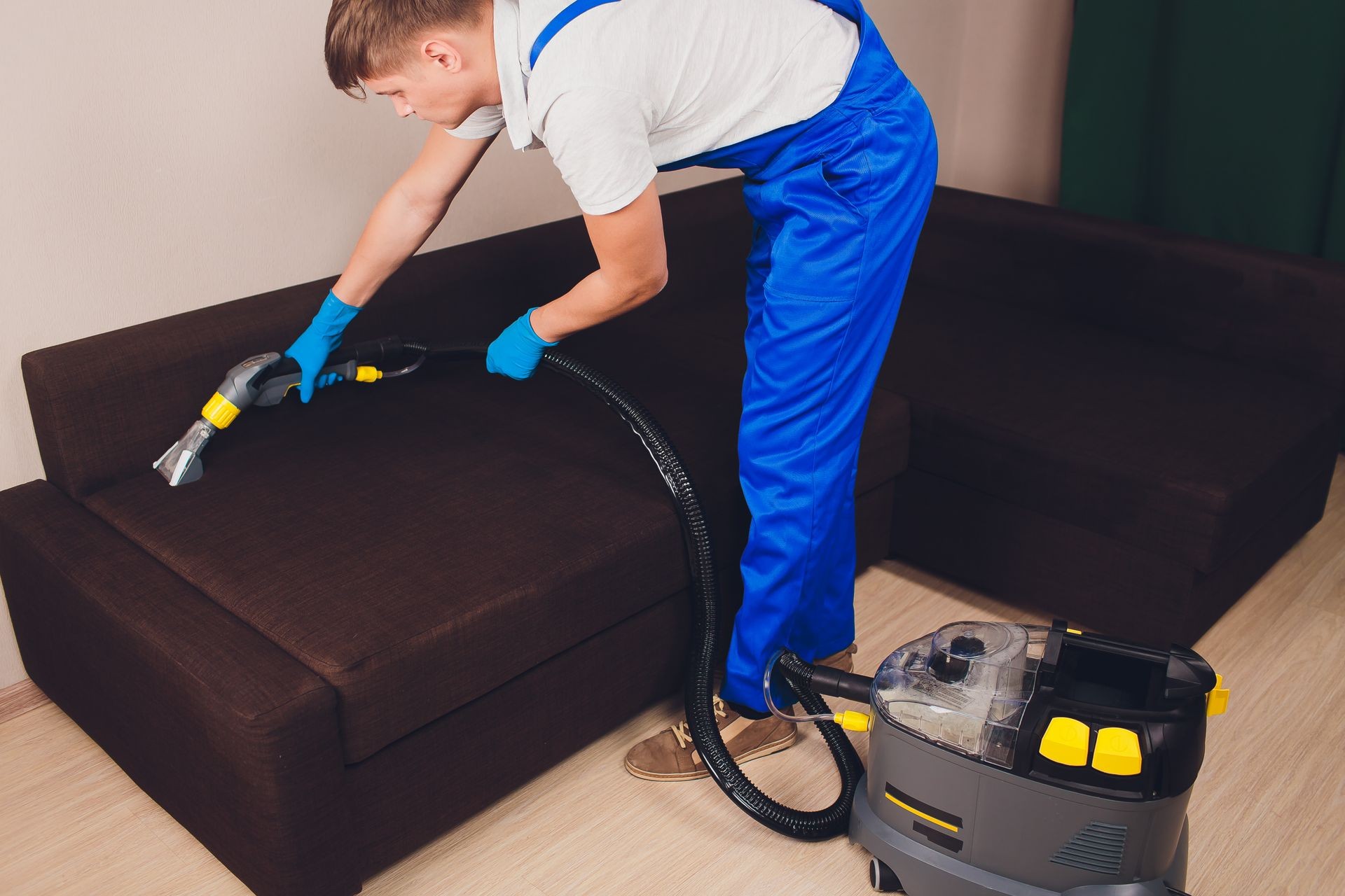 Sofa chemical cleaning with professionally extraction method. Upholstered furniture. Early spring cleaning or regular clean up. Dry cleaner's in light blue protective glove employee removing dirt from